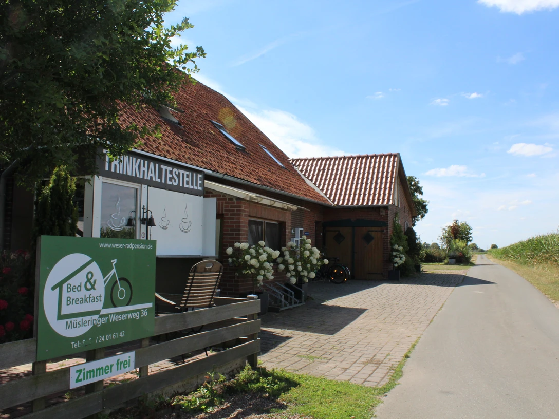 Eingang eines Backsteinhauses an ruhiger Landstraße, Fahrradverleih und Übernachtungsmöglichkeiten.