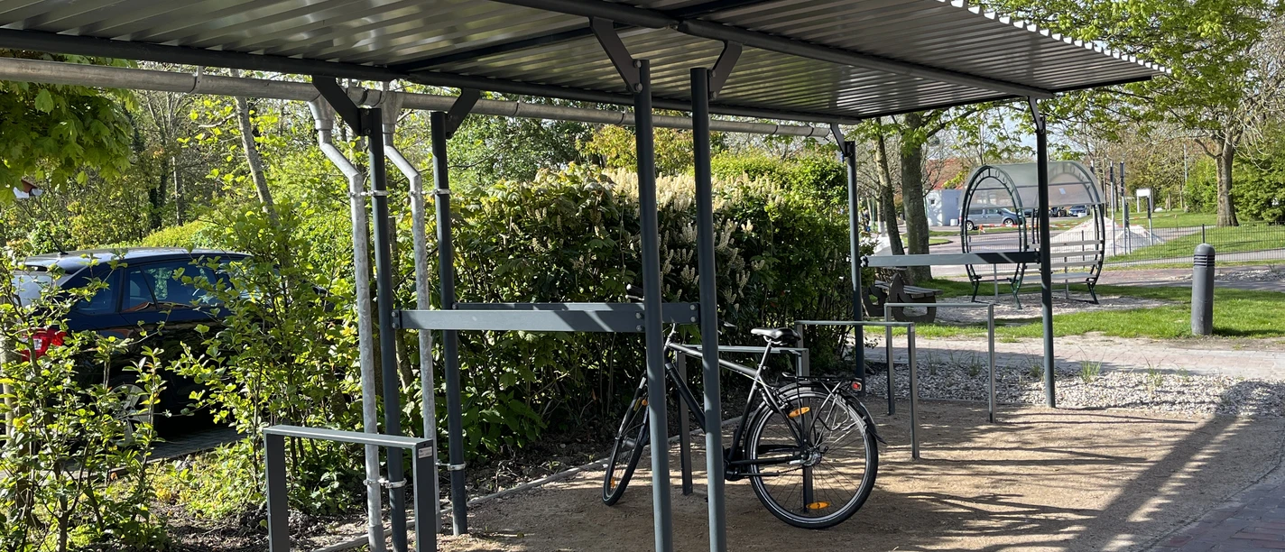 Fahrradparkplatz Zur Hauener Hooge in Greetsiel Überdachter Fahrradparkplatz mit Metallgestell, geparktem Rad und umliegendem Grün in Greetsiel