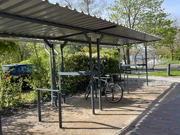 Fahrradparkplatz Zur Hauener Hooge in Greetsiel Überdachter Fahrradparkplatz mit Metallgestell, geparktem Rad und umliegendem Grün in Greetsiel