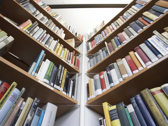 Stadtbücherei Bad Oeynhausen Zwei Reihen von Bücherregalen voller farbiger Bücher, fotografiert aus einem niedrigen Blickwinkel.