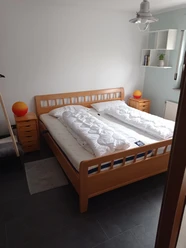 Helles Schlafzimmer mit einem Doppelbett aus Holz, zwei Nachttischen und einer Stehlampe rechts.