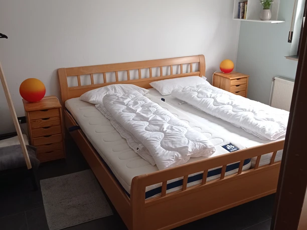 IMG_20230412_143709.jpg Helles Schlafzimmer mit einem Doppelbett aus Holz, zwei Nachttischen und einer Stehlampe rechts.