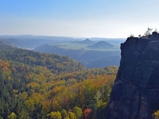 Aussicht Breite Kluft Blick auf eine herbstlich gefärbte Waldlandschaft mit einem markanten Felsen im Vordergrund und sanften Hügeln im Hintergrund unter klarem Himmel.