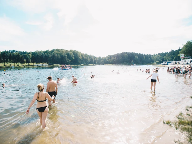 ErnestoUhlmann_StauseeOberrabenstein.jpg Menschen genießen einen sonnigen Tag am Stausee, schwimmen und entspannen am Sandstrand.