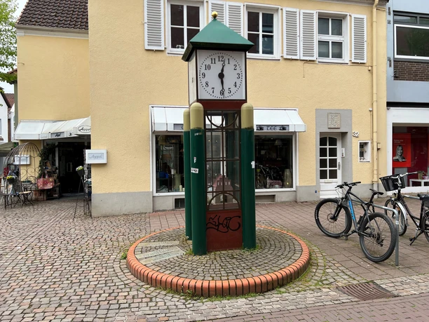 Eine in ein Uhrwerk integrierte Kunststoffspargel-Statue mit umgebenden Geschäften und Fahrrädern.