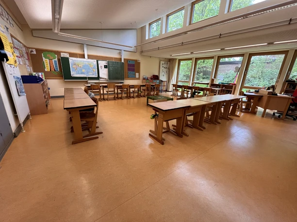 IMG_0758.jpg Heller Klassenraum der Grundschule Amelinghausen mit Holztischen, Stühlen und großen Fensterfronten.