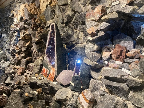 Various types of stone and crystals are displayed in a stone wall, including a large, purple amethyst with lighting.