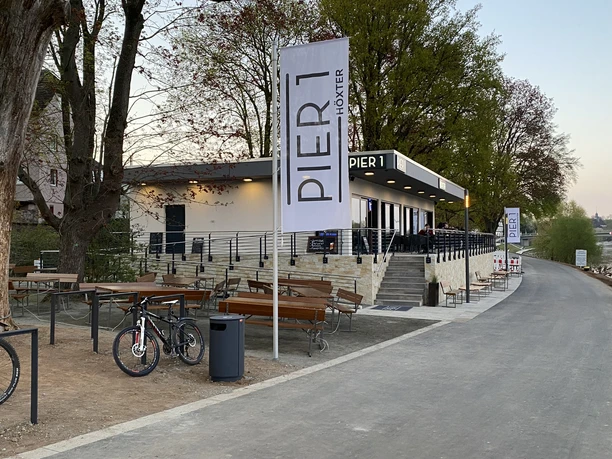 Pier1_Ansicht außen ohne Personen.jpg Flachdachbau mit Gastronomie Pier1 am Weser-Radweg mit Außensitzplätzen
