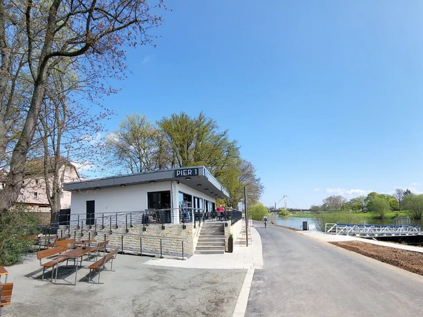 Pier1_Ansicht II außen ohnen Personen.jpg Flachdachbau mit Gastronomie Pier1 am Weser-Radweg mit Außensitzplätzen