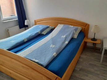 Dreppenstedt Ein Doppelbett mit blauem Bettzeug in einem hellen Zimmer, ergänzt durch zwei Nachttische mit Lampen.