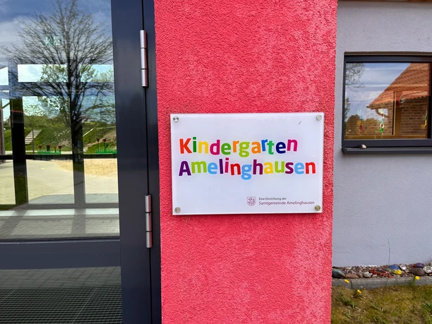 Kindergarten Amelinghausen Eingang Eingangsbereich mit buntem Schild Kindergarten Amelinghausen an pinker Wand.