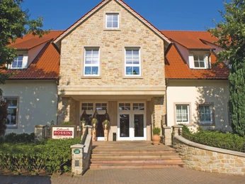 Halle-EingangRossini-TeutoburgerWald-mayfeldWerbeagentur-HenningMayer.jpg Traditionelles zweistöckiges Haus mit Sandsteinfassade und rotem Dach, Restaurant Rossini-Schild.