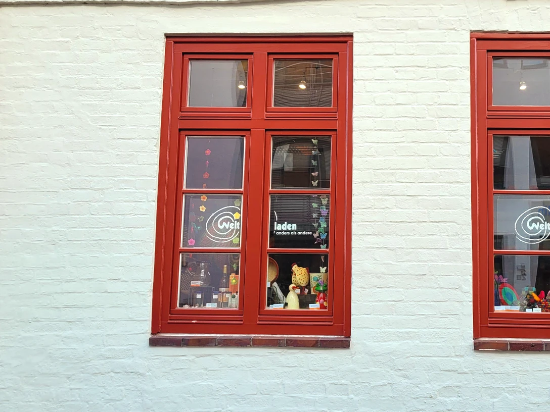 Weltladen Esperanza_Silvana Dust_20230510 (3).jpg Vom Gebäude sind zwei rote Fenster mit dem Aufdruck ‚Weltladen‘ zu sehen