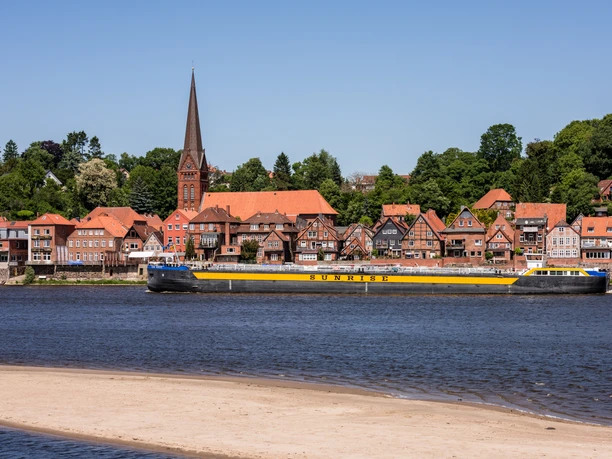 Blick auf Elbe und Lauenburg Ein Schiff fährt auf einem Fluss. Am Ufer steht eine Stadt mit einer Kirche.