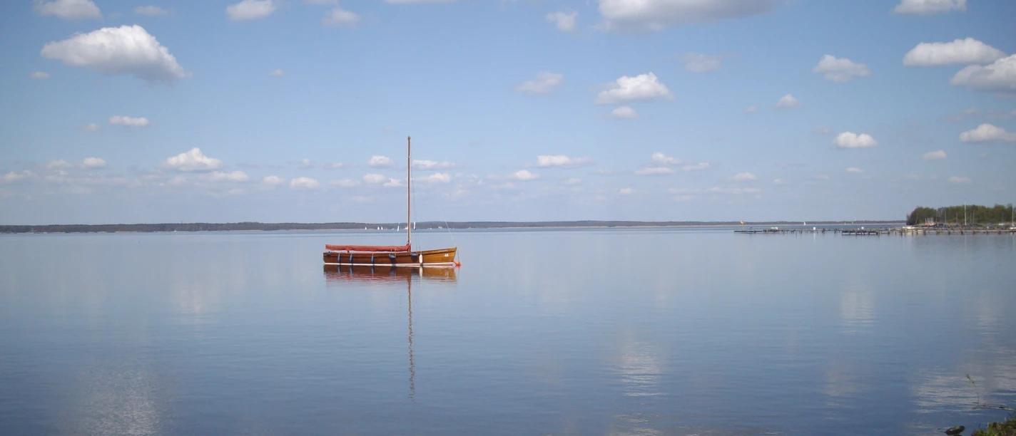 A single sailing boat rests peacefully on a wide, calm lake under a clear blue sky.