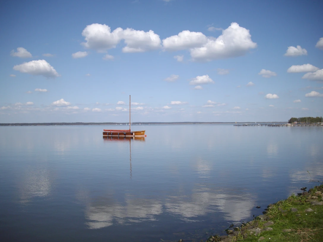 Steinhuder Meer.JPG Ein einzelnes Segelboot ruht friedlich auf einem weiten, stillen See unter klarem blauem Himmel.