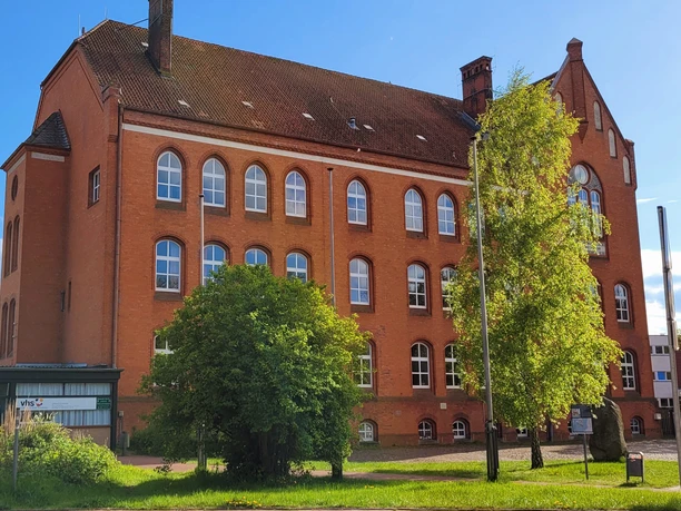 Volkshochschule_Silvana Dust_20230510_1980x1310.jpg Außenansicht der Volkshochschule Ratzeburg mit Eingangsbereich, Fenstern und umliegendem Gehweg sichtbar