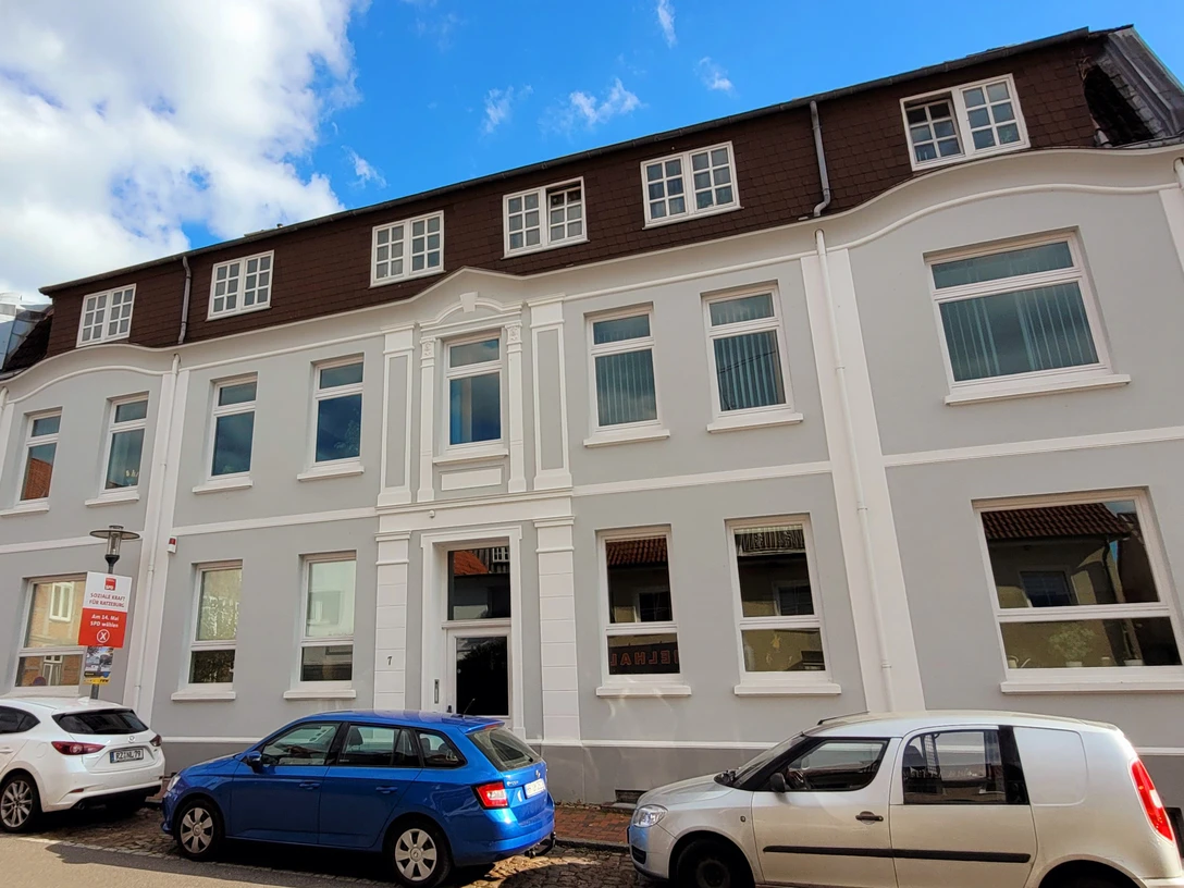 Stadtarchivar_Silvana Dust_20230510_1980x1310.jpg Ein Haus mit hellgrauem Anstrich und Seitenstreifen, davor parkende Autos