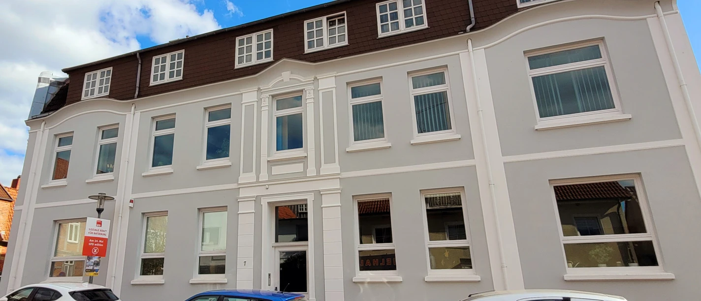 Stadtarchivar_Silvana Dust_20230510_1980x1310.jpg Ein Haus mit hellgrauem Anstrich und Seitenstreifen, davor parkende Autos