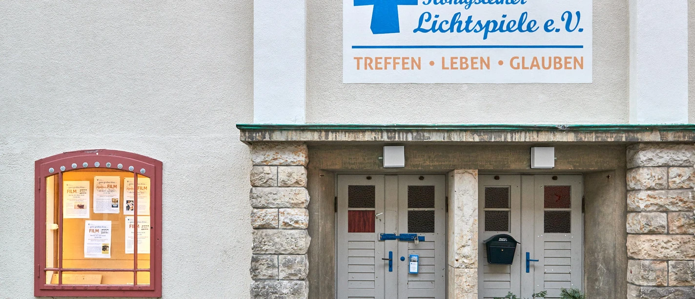 Entrance of the Königsteiner Lichtspiele e.V. with a sign "Treffen, Leben, Glauben" and a showcase with movie announcements.