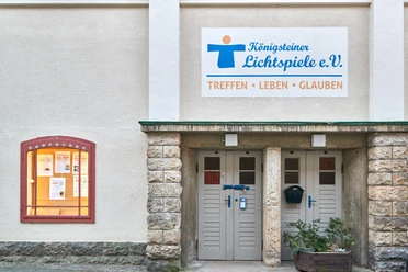Königsteiner Lichtspiele e.V. Eingang der Königsteiner Lichtspiele e.V. mit einem Schild "Treffen, Leben, Glauben" und einem Schaukasten mit Filmankündigungen.