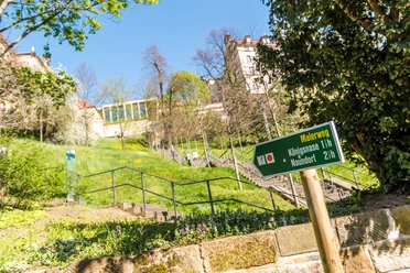 Terrassengärten Schloss Pirna Grünes Schild mit der Aufschrift "Malerweg" zeigt Wanderzeiten an, im Hintergrund eine Treppe und ein historisches Gebäude bei sonnigem Wetter.