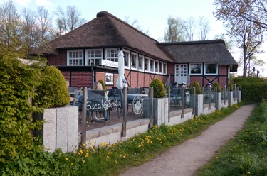 Eiscafé Bruhn_Silvana Dust_20230510_1980x1310.jpg Blick auf Sitzplätze vor einem Eiscafé, an denen Besucher sitzen