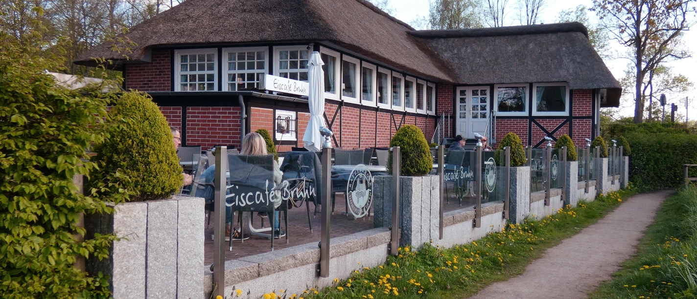 Eiscafé Bruhn_Silvana Dust_20230510_1980x1310.jpg Blick auf Sitzplätze vor einem Eiscafé, an denen Besucher sitzen