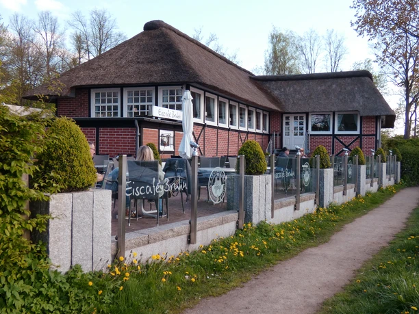 Eiscafé Bruhn_Silvana Dust_20230510_1980x1310.jpg Blick auf Sitzplätze vor einem Eiscafé, an denen Besucher sitzen