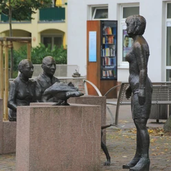 Skulpturengruppe mit Menschen aus Bronze, die rund um einen Tisch sitzen, im Freien positioniert.