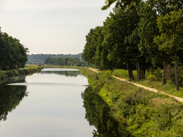 Der Elbe-Lübeck-Kanal. Auf der rechten Seite ist der Radfernweg "Alte Salzstraße" zu sehen. Bäume säumen beide Seiten des Kanals.