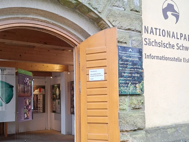 Toegang tot het informatiecentrum van het ijshuis in het Nationaal Park Sächsische Schweiz met open houten deuren en informatieborden binnenin.