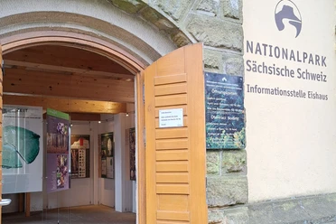 Eingang zur Infostelle Eishaus Eingang zur Informationsstelle Eishaus im Nationalpark Sächsische Schweiz mit offenen Holztüren und Infotafeln im Inneren.