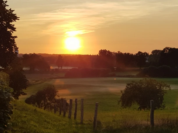 Stecknitzniederung Ein Blick über die Stecknitzniederung bei Sonnenuntergang. Die Landschaft ist grün. Über den Wiesen liegt leichter Nebel. Im Vordergrund sieht man einen Zaun.