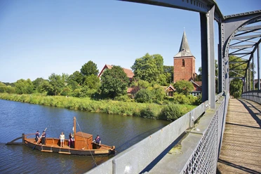 Auf den Spuren der Stecknitzfahrer Von der Kirchsteigbrücke aus blickt man auf ein Boot mit Menschen auf dem Elbe-Lübeck-Kanal. Am Ufer steht die Maria-Magdalenen-Kirche in Berkenthin.