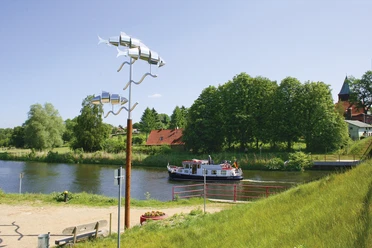 Kornbrennerweg Ein Schiff fährt auf dem Elbe-Lübeck-Kanal bei Krummesse. Am Ufer stehen grüne Bäume und eine Kirche. Die Sonne scheint.