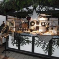 Adventskrämchen.jpg Festlich geschmückter Weihnachtsmarktstand, dekoriert mit Tannenzweigen und glitzerndem Stern.