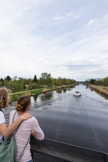 Zwei Frauen schauen von einer Brücke auf das Wasser. Dort fährt ein kleines Boot.