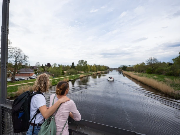 Zwei Frauen schauen von einer Brücke auf das Wasser. Dort fährt ein kleines Boot.