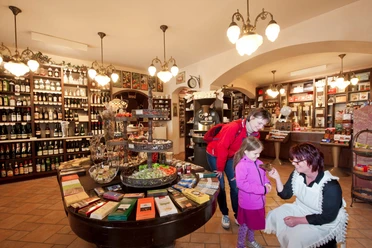 Schmole coffee roastery A cozy store with shelves full of bottles of wine; a woman in an apron shows a child in a pink jacket something while another woman looks on.