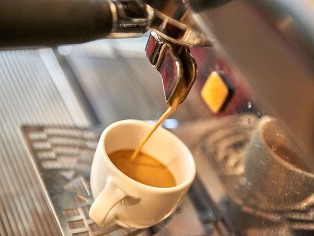 Kaffeerösterei Schmole Espresso fließt aus einer Siebträgermaschine in eine weiße Tasse, die auf einem Metallgitter steht.