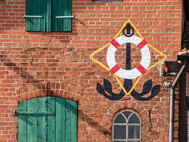 Backsteingebäude mit Straßenkunst in Lauenburg Eine Hauswand aus roten Backsteinen. Darauf ist ein Rettungsring und ein Anker gemalt.