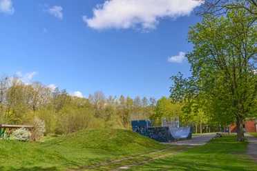 Blomberg_JUZ_Scaterbahn_2216_RHa.jpg Skaterbahn in grüner Parksze, umgeben von Bäumen, mit einer Halfpipe und blauem Himmel im Hintergrund.