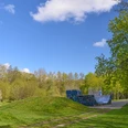 Blomberg_JUZ_Scaterbahn_2216_RHa.jpg Skaterbahn in grüner Parksze, umgeben von Bäumen, mit einer Halfpipe und blauem Himmel im Hintergrund.