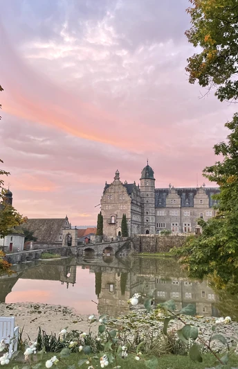 Schloss Hämelschenburg spiegelt sich im Teich, umrahmt von herbstlich gefärbten Bäumen bei Sonnenuntergang.