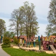Spielplatz in einem parkähnlichen Gelände mit Piratenschiff-Klettergerüst und umstehenden Bäumen.