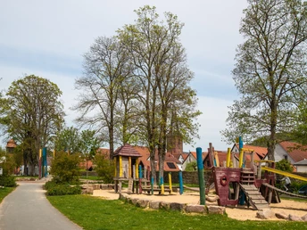 Spielplatz in einem parkähnlichen Gelände mit Piratenschiff-Klettergerüst und umstehenden Bäumen.