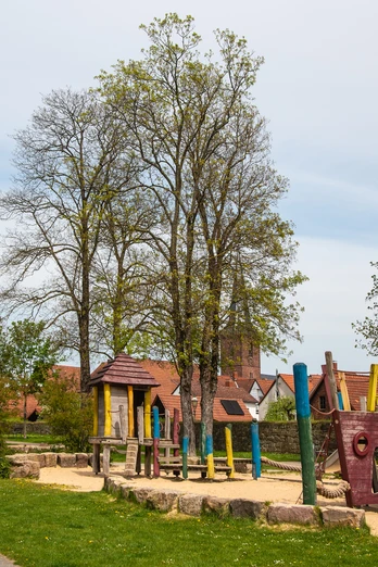 Spielplatz in einem parkähnlichen Gelände mit Piratenschiff-Klettergerüst und umstehenden Bäumen.