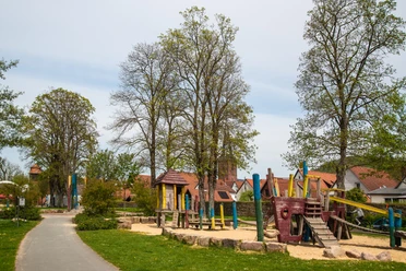 Spielplatz in einem parkähnlichen Gelände mit Piratenschiff-Klettergerüst und umstehenden Bäumen.