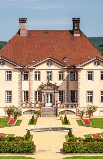 Vor einem bewaldeten Hügel erhebt sich ein elegantes Herrenhaus mit symmetrischer Gartenanlage.
